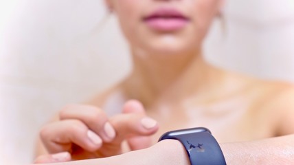 Attractive young woman athlete wearing and using smartwatch in bathroom. Taping smartwatch device screen.