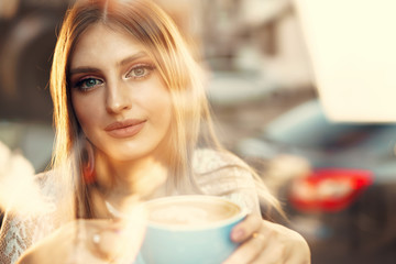 Portrait of a young woman having a cup of coffee and looking through the window