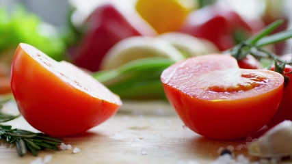 Tomato cut exactly in half on a wooden board in the kitchen next to other vegetables