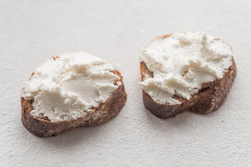 Whole grain bread bruschetta with white soft curd cream cheese on a white background. Close-up