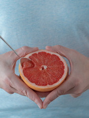 Closeup, photo of a woman holding half of fresh ripe red grapefruit in her hand. Blue pastel background. Copy space mockup. Vertical orientation. Tasty, healthy desser
