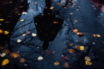 Reflection of a person in a puddle of water under the rain
