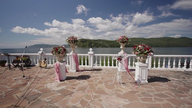 wedding aisle setup on lake or sea shore promenade. outside ceremony, celebration. flower decoration. Rows of white empty chairs. concert guitar music equipment. concept nobody