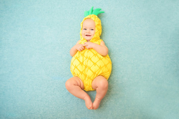 Cute smiling baby in a pineapple costume lies on a blue background