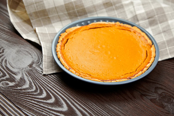 Pumpkin pie in baking tray, kitchen towel on brown wooden table