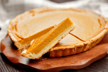 Thanksgiving pumpkin pie on cutting board on brown wooden table. Piece of pie