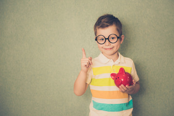 Boy in glasses with piggy bank against blue background, space for text. Business and saving money...