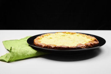 Cooked omelet in a black plate, green kitchen towel on white table on black background. Omelette from chicken eggs