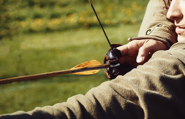 detail of a woman training shooting with a bow on a meadow,