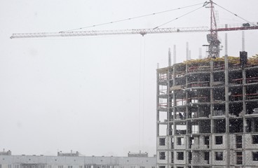 home building with crane on gray sky background in snowy weather