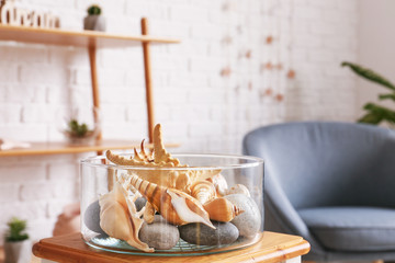 Vase with sea shells on table in room