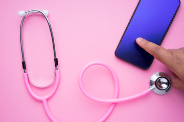 Fototapeta premium Technology in women healthcare concept. A pink stethoscope and a smartphone on a pink background. Landscape orientation.