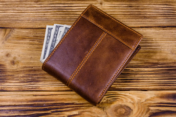 Brown leather wallet and one hundred dollar banknotes on the wooden background