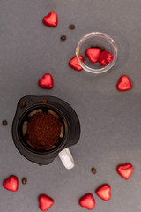 That's ground coffee in a strainer over the cup on a dark background with grains and red hearts. The top view. Flat lay.