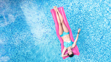 Beautiful young woman in hat in swimming pool aerial top view from above, young girl in bikini relaxes and swims on inflatable mattress and has fun in water on family vacation, tropical holiday resort