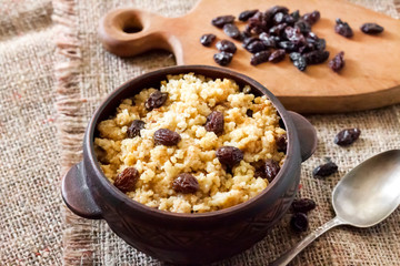 Sweet millet porridge with dark raisins in ceramic rustic bowl