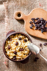 Sweet millet porridge with dark raisins in ceramic rustic bowl