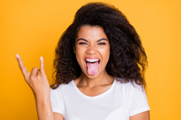 Photo of curly wavy excited crazy screaming girl sticking tongue out with horned fingers rock sign screaming isolated in white t-shirt vibrant color background