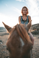 a young girl with red hair sees riding a red horse at sunset along a hill scorched by the sun against a background of high snow peaks - 316955133