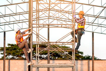 Fototapeta premium Technicians in safety clothing are climbing scaffolding. Friends go up and check the strength of the metal roof part of the building.