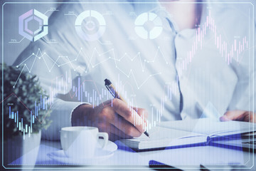 Double exposure of man's hands writing notes of stock market with forex chart.