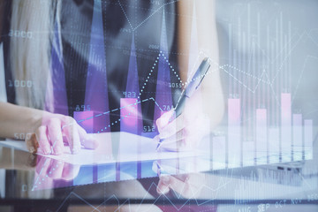 A woman hands writing information about stock market in notepad. Forex chart holograms in front. Concept of research.