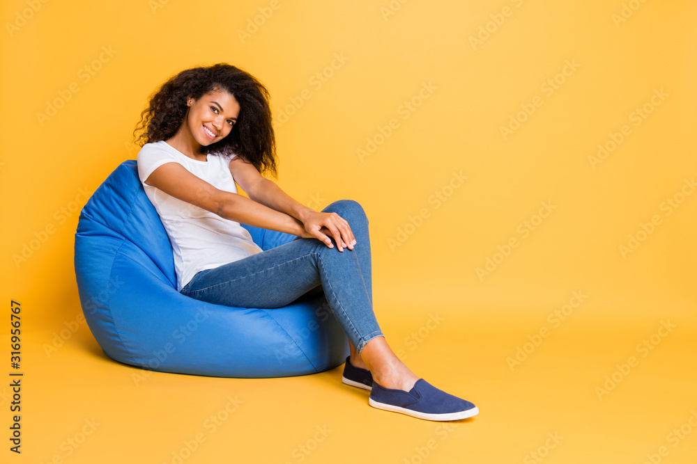 Sticker Full length body size turned photo of cheerful positive cute nice pretty attractive black youngster wearing jeans denim white t-shirt sitting in bean near empty space isolated vivid color background