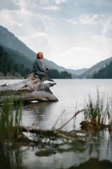 red-haired girl sits on a dry tree in the middle of a clean transparent lake, around the mountains, ns of the sky soft diffused light falls - 316956797