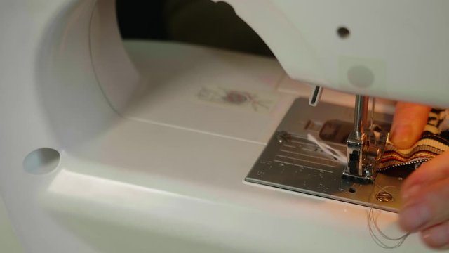 Close up of woman's hands sewing little grey fabric on electrical sewing machine and then take it out of sweing machine.