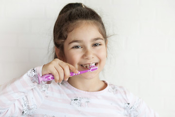 Happy cute little child girl brushing her teeth on light background. Space for text. Healthy teeth.