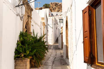 Fototapeta na wymiar Narrow street in old town. Beautiful street with white buildings in Lindos Greece. 
