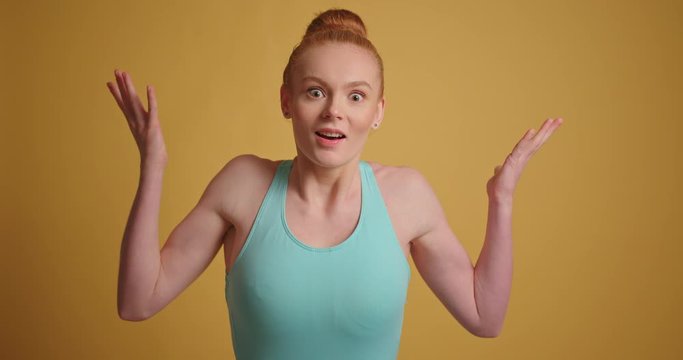 Joyful redhead girl hands gesticulating interrogative asking why at yellow background
