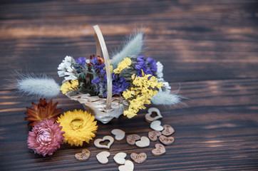 Basket with dried flowers and hearts around on a wooden table top.