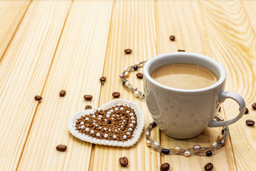 Valentine's Day concept. Cup of coffee, knitted heart, string of pearl beads. Romantic breakfast and gift on wooden boards background