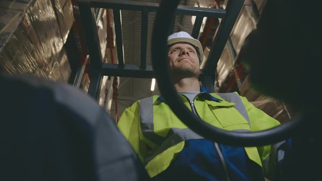 Bottom view of male staff driving forklift in warehouse. Worker on a loader in a storehouse