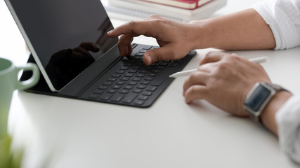 Cropped shot of businessman typing on tablet keyboard in simple workspace with coffee cup and office supplies