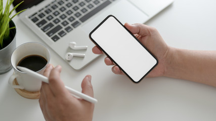 Overhead shot of businessman using smartphone in modern workspace with laptop, coffee cup and other office supplies
