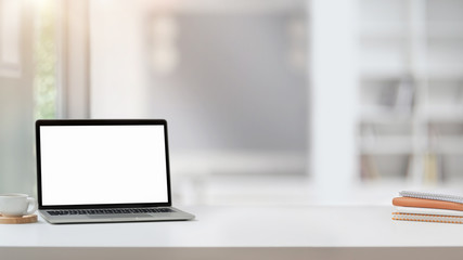 Close up view of workplace with blank screen laptop, copy space, notebooks and coffee cup on white table