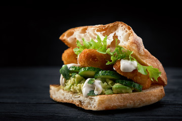 Sandwich with nuggets salad leaves and sauce on a dark wooden background. fast food, street food, copy space, dark background.