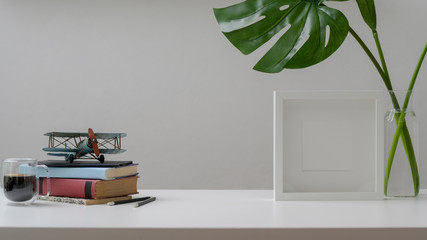 Close up view of workspace with copy space, books, mock up frame and decorations on white wooden desk