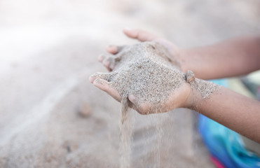 Sand puffs through the fingers of a girl's hand.