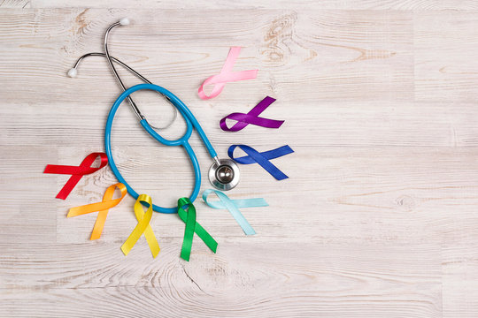 Colorful awareness ribbons with a stethoscope on wooden table. World cancer day concept, February 4.