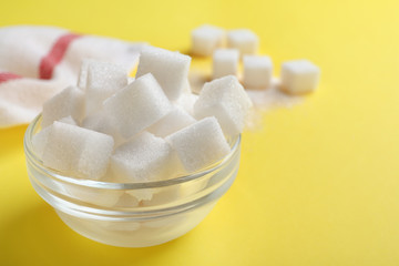 Refined sugar cubes in glass bowl on yellow background