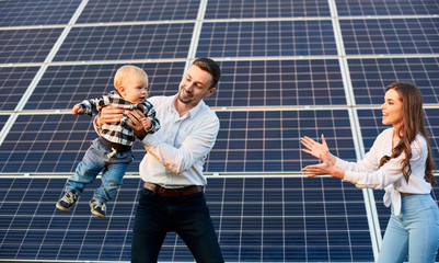 Happy young family with a little blond child having fun on the background of solar panels. A modern...