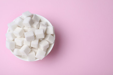 Refined sugar cubes in bowl on pink background, top view. Space for text