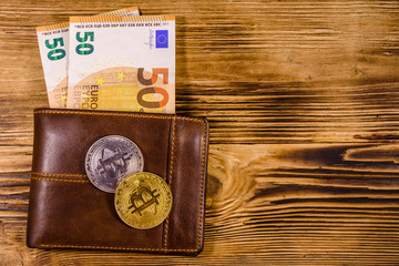 Brown leather wallet with fifty euro banknotes and bitcoins on the wooden background. Top view