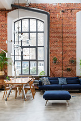 Spacious interior of living room in loft apartment with big window, red brick wall and navy sofa with pillows. Minimal and contemporary architecture in lounge. 3d vertical.