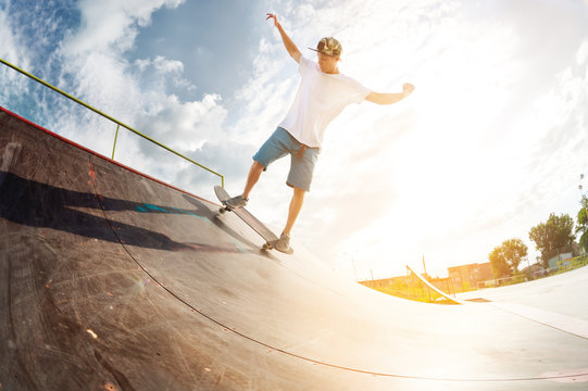 Portrait of a young skateboarder doing a trick on his skateboard on a halfpipe ramp in a skate park in the summer on a sunny day. The concept of youth culture of leisure and sports