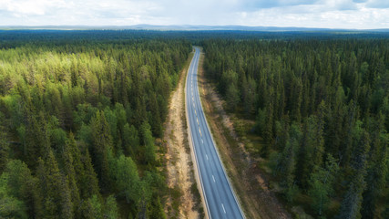 Aerial view from above of country road through the green summer fir forest in summer Lapland. Drone photography.