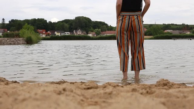 Woman walking into lake, sand beach. Solo woman traveler.